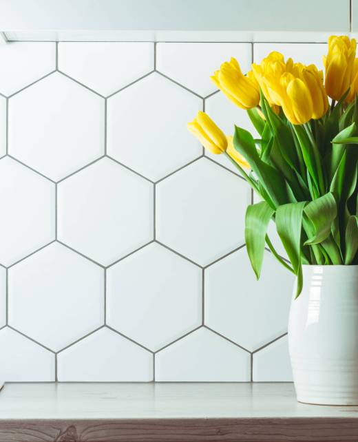 Interior shot. Yellow tulip bouquet in white vase on kitchen countertop on hexagonal white tile background, copy space